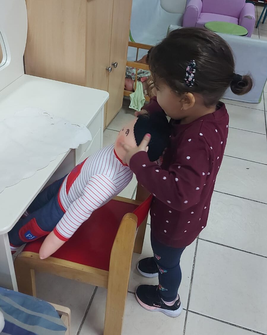 ילדה משחקת עם בובה ומושיבה אותה על כיסא